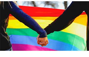 Two people holding hands in front of a rainbow flag